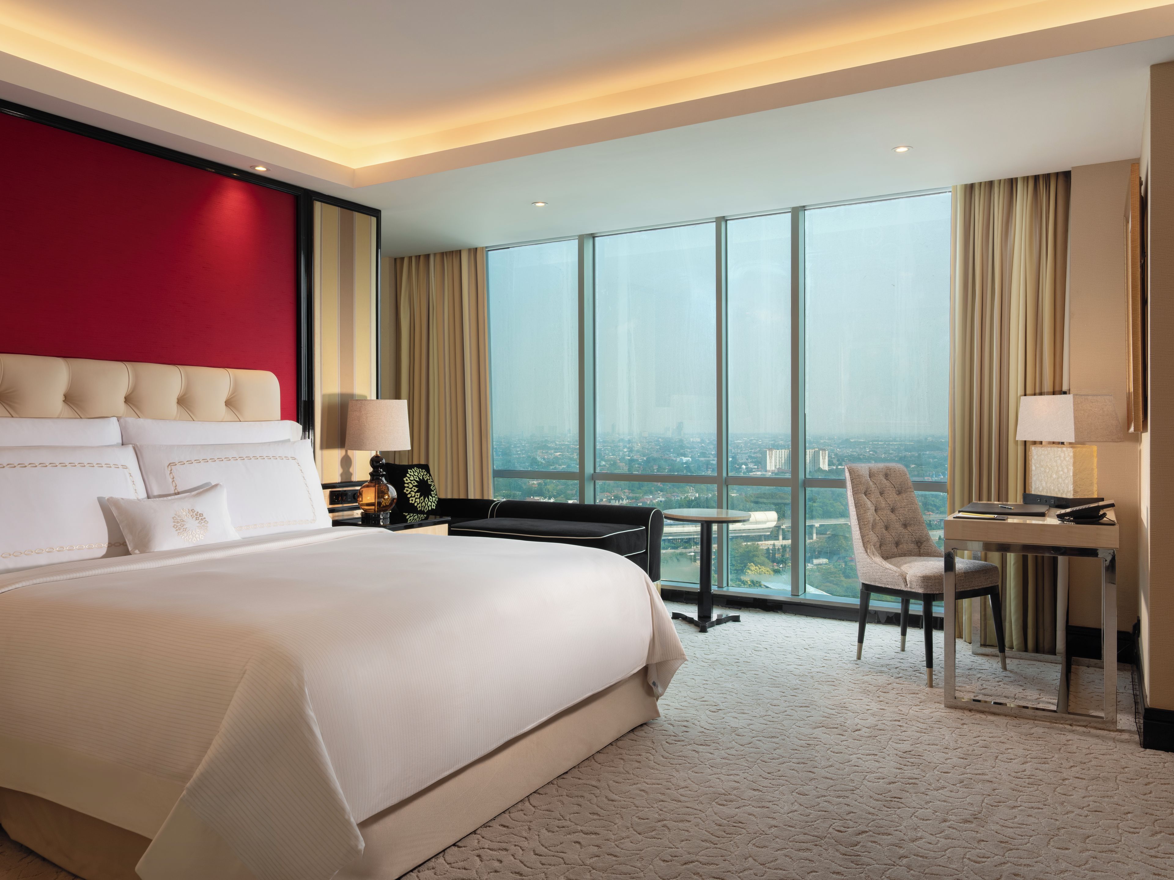 A hotel room with a large bed, a desk, a chair, and a view of the city.