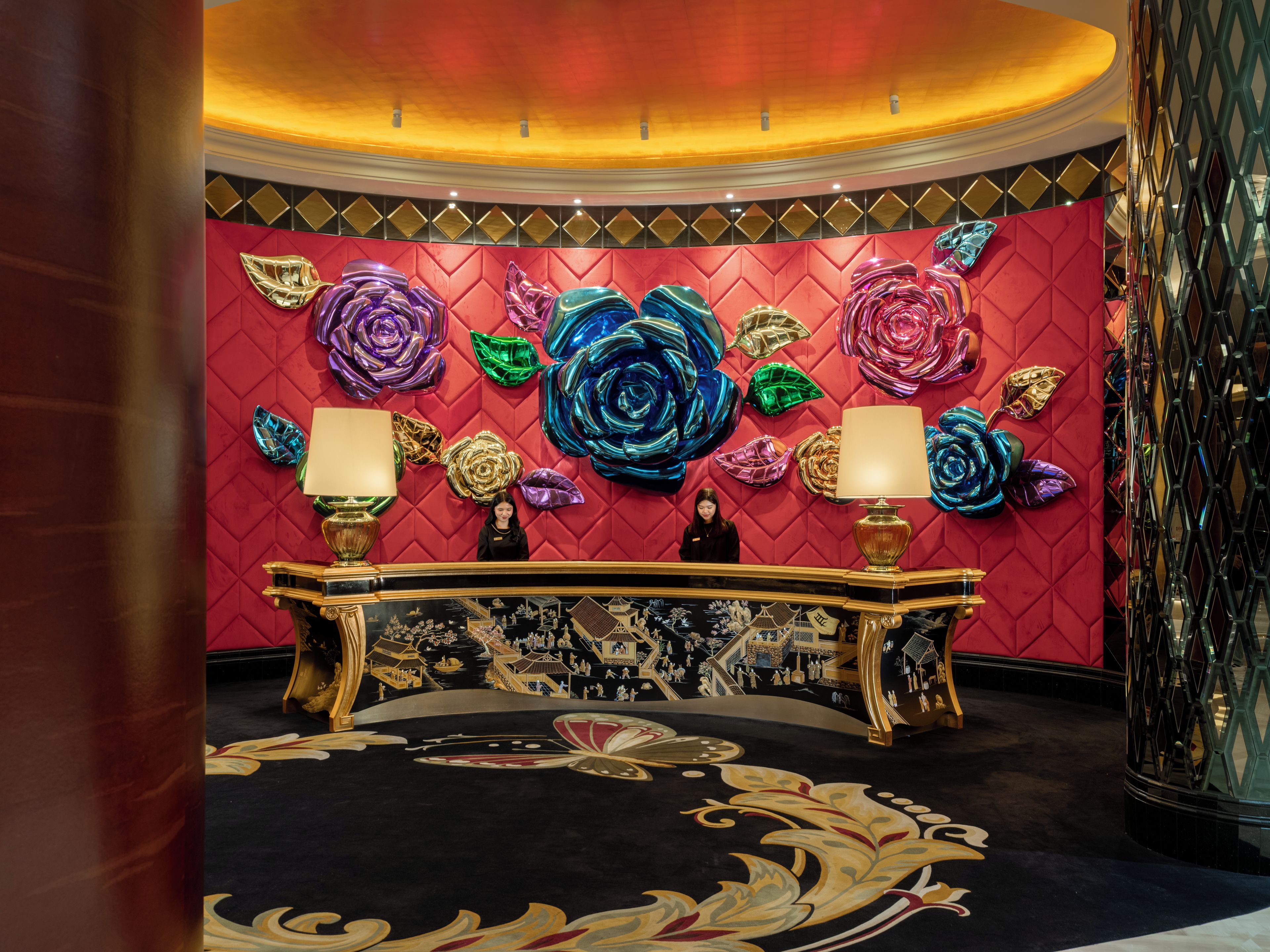 A lobby with a red wall, a large ornate desk, and a patterned carpet.