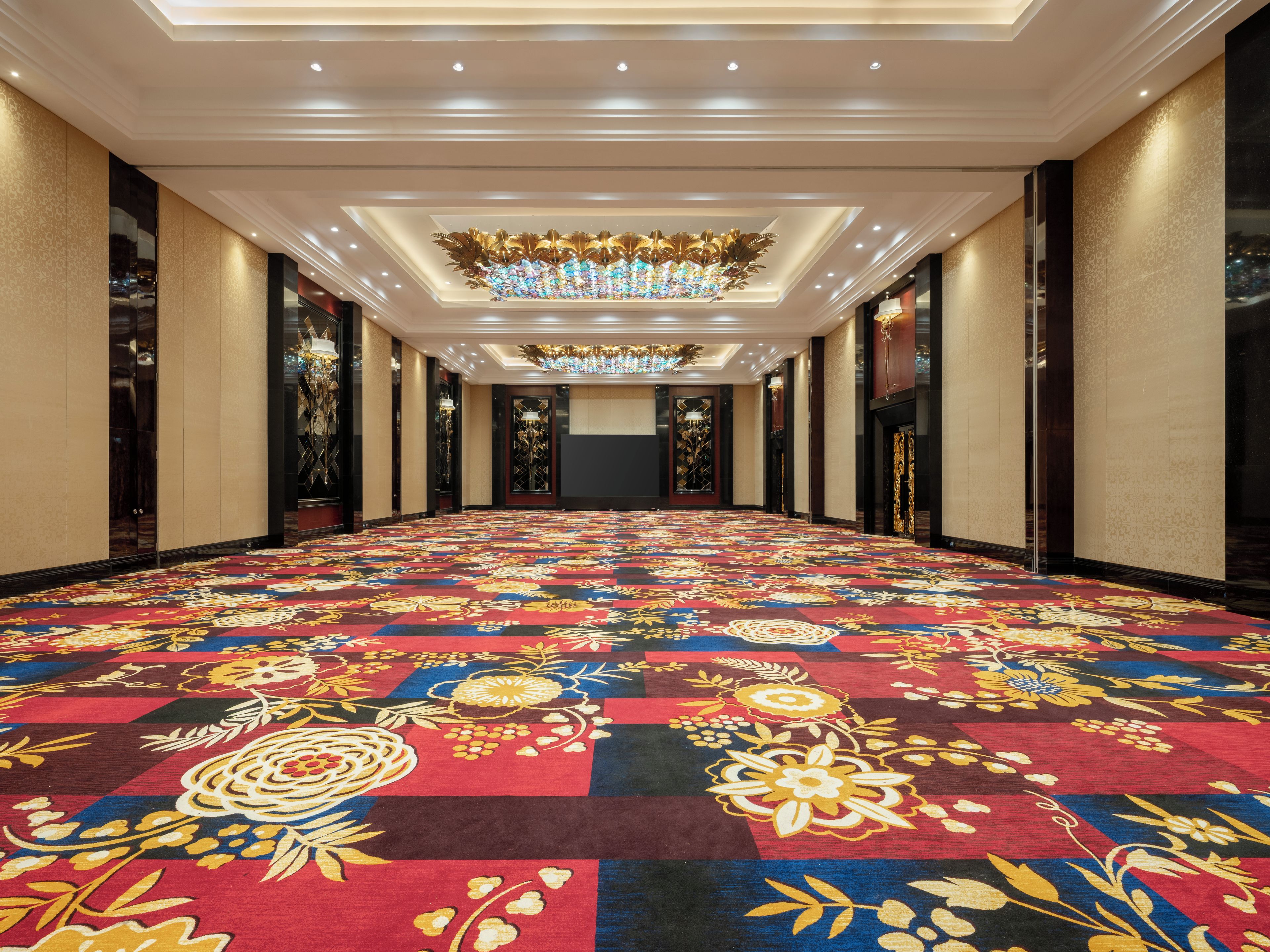 Een hotelgang met een kamerjas patroon, versierd plafond en een grote kroonluchter.