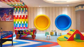 A children's play area with a foosball table, colorful play structures, and a wall with a checkered pattern.
