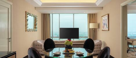 A hotel room with a dining area, a sofa, a TV, and a view of the city.