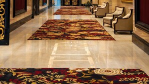 Un vestíbulo de hotel con una lámpara de araña imponente, puertas rojas y una alfombra estampada.