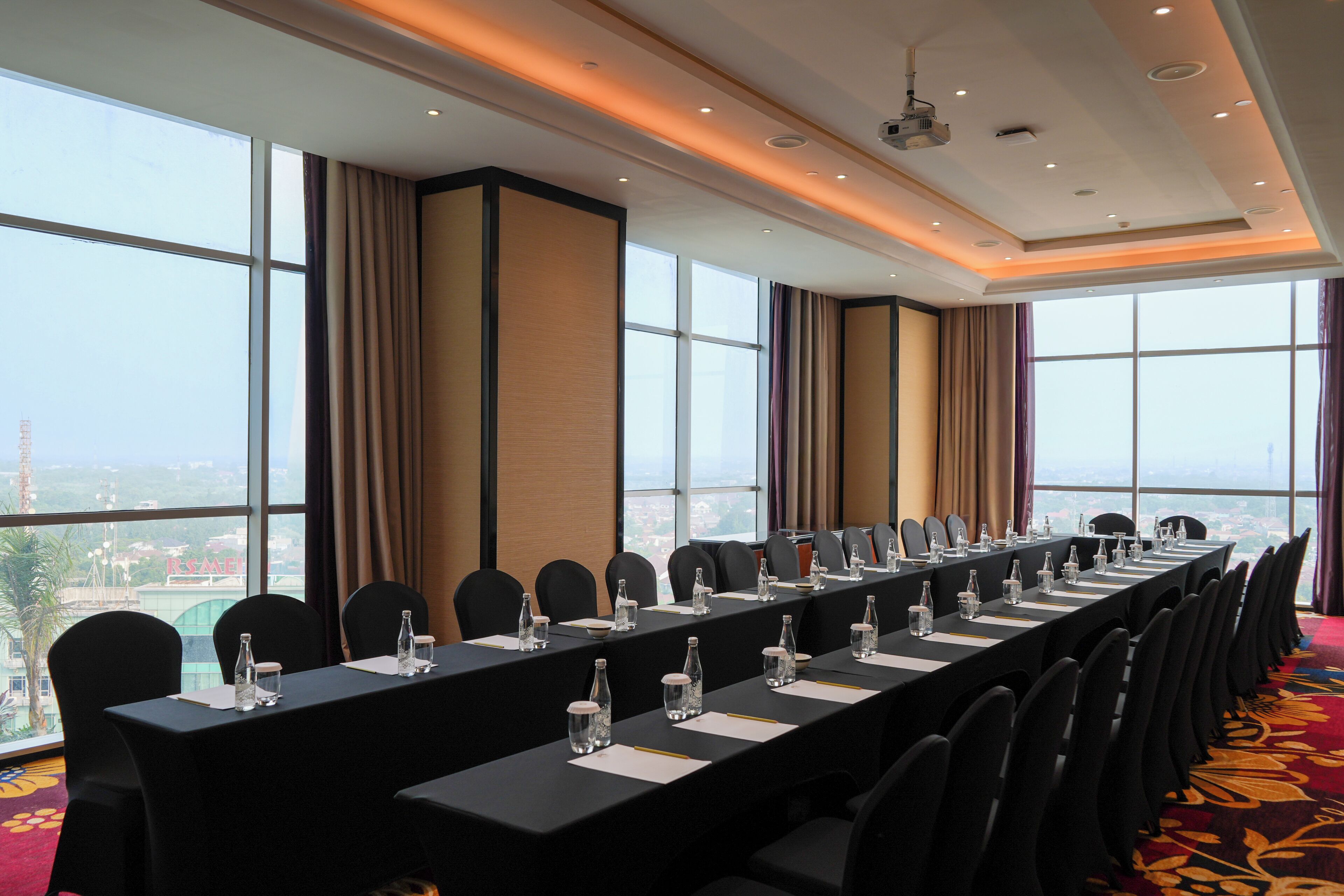 Un salón de conferencias con una larga mesa, sillas y vistas a la ciudad a través de amplias ventanas.