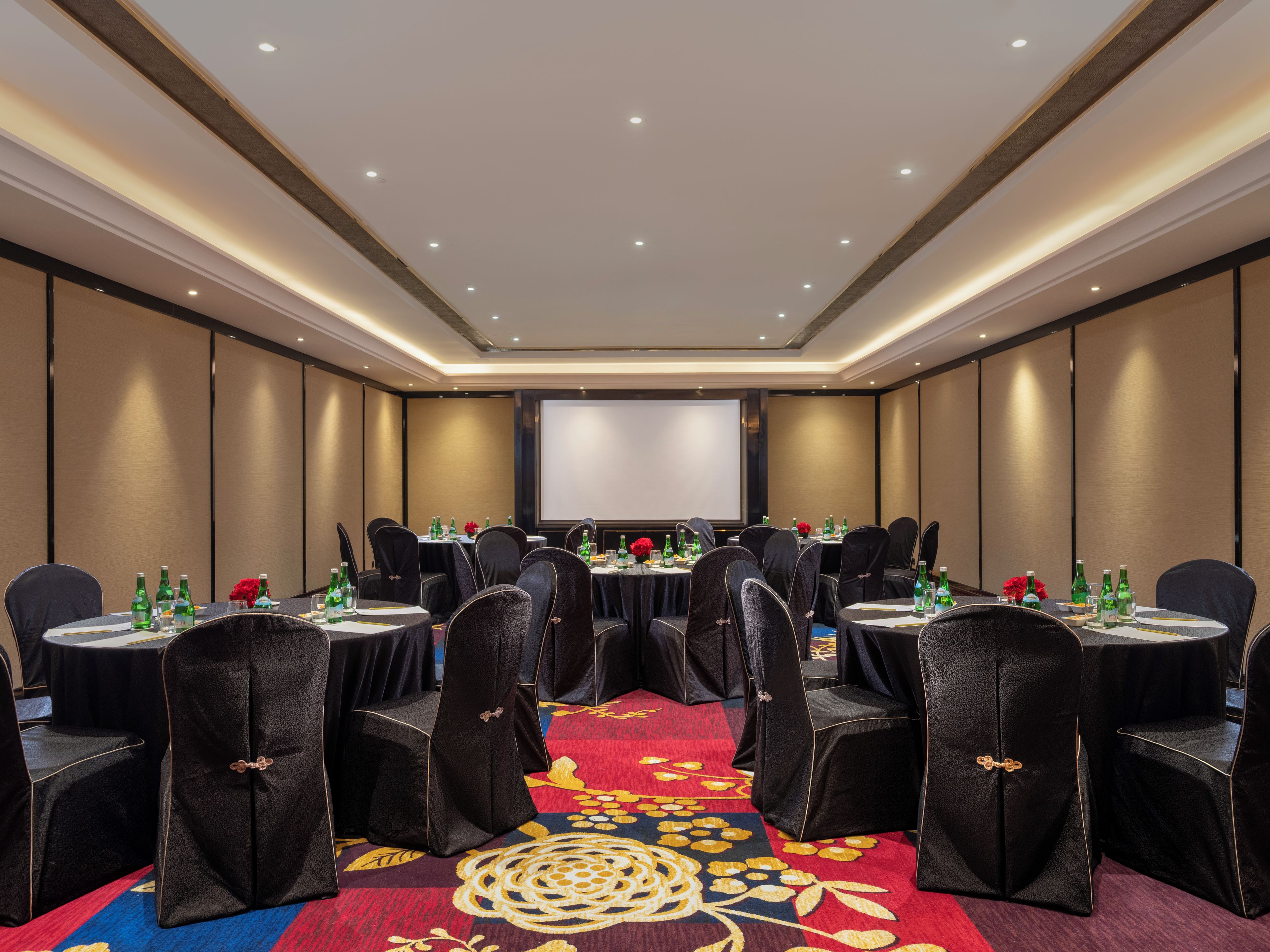 A conference room with round tables, chairs, and a projector screen.