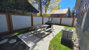 Patio trasero con parrilla, mesa de picnic y unidad de aire acondicionado.