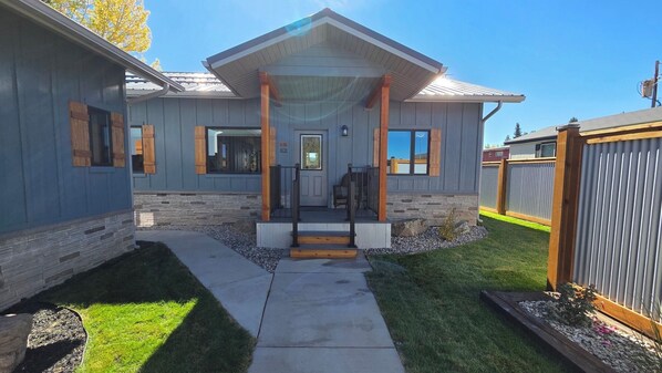 A modern two-story house with a stone foundation, a covered front porch, and a well-maintained lawn. - Parkside Cabins - Yellowstone vacation get-away. Newly built, very private. (West Yellowstone)