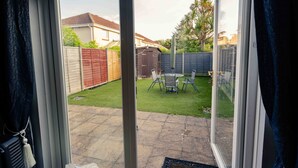 A view through a glass door into a backyard with a patio area, a wooden fence, and a small shed. - House - Sleeps 8 - Pet friendly - Garden - Parking (Andover)