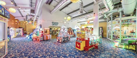 An indoor arcade with various gaming machines, a shop sign, and a patterned carpet.