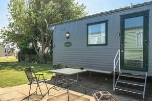 A mobile home with a patio area, a table, two chairs, and a small set of steps leading to the door. - 3 Bed Caravan - Sleeps 8 - Pets - Garden - Parking (Hull)