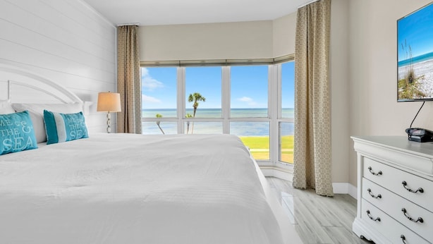 Een hotelkamer met een groot bed, een televisie en uitzicht op het strand.