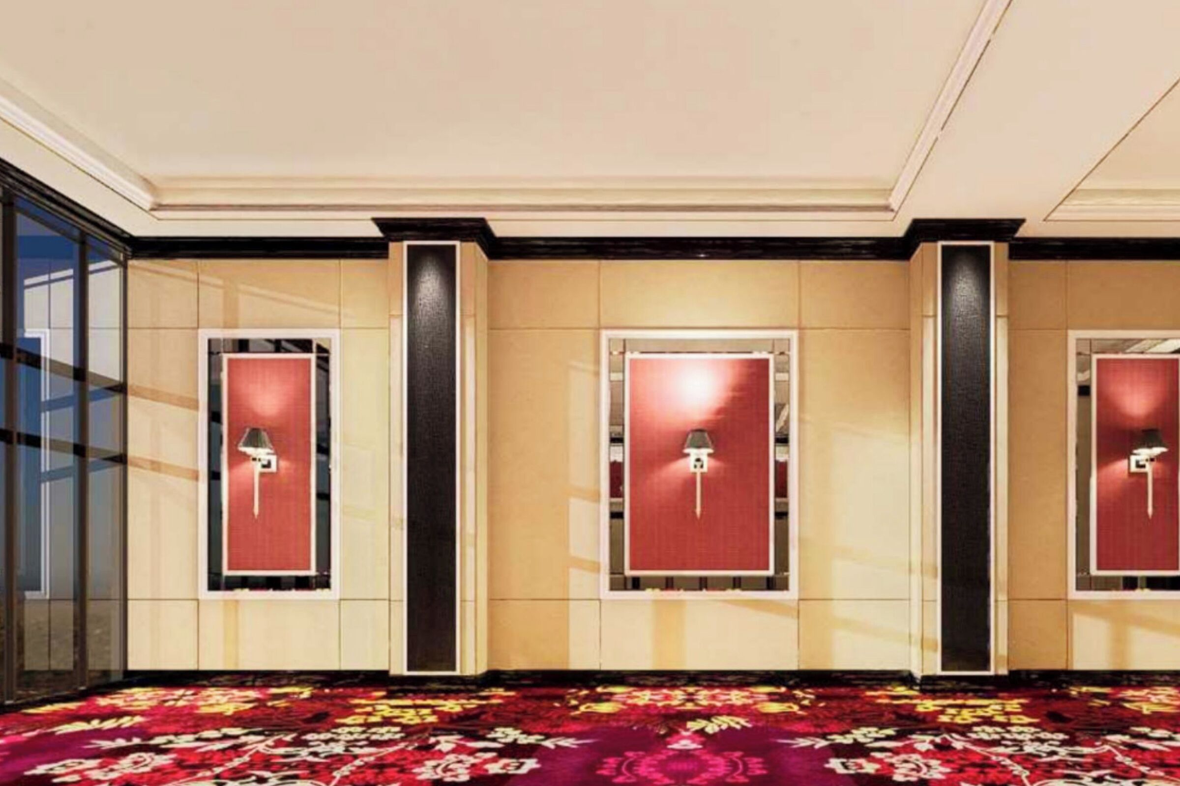 Un hall de hotel con tres puertas, cada una con un panel rojo y una lámpara arriba. El piso está cubierto por una alfombra estampada.