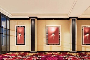A hotel lobby with three doors, each with a red panel and a light fixture above. The floor is covered with a patterned carpet.