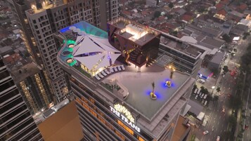 Un hotel de gran altura con varios pisos, una terraza en la azotea con sombrillas y una piscina.