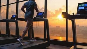 Una persona usando una cinta de correr en una habitación con amplias ventanas que dan a un paisaje urbano al atardecer.