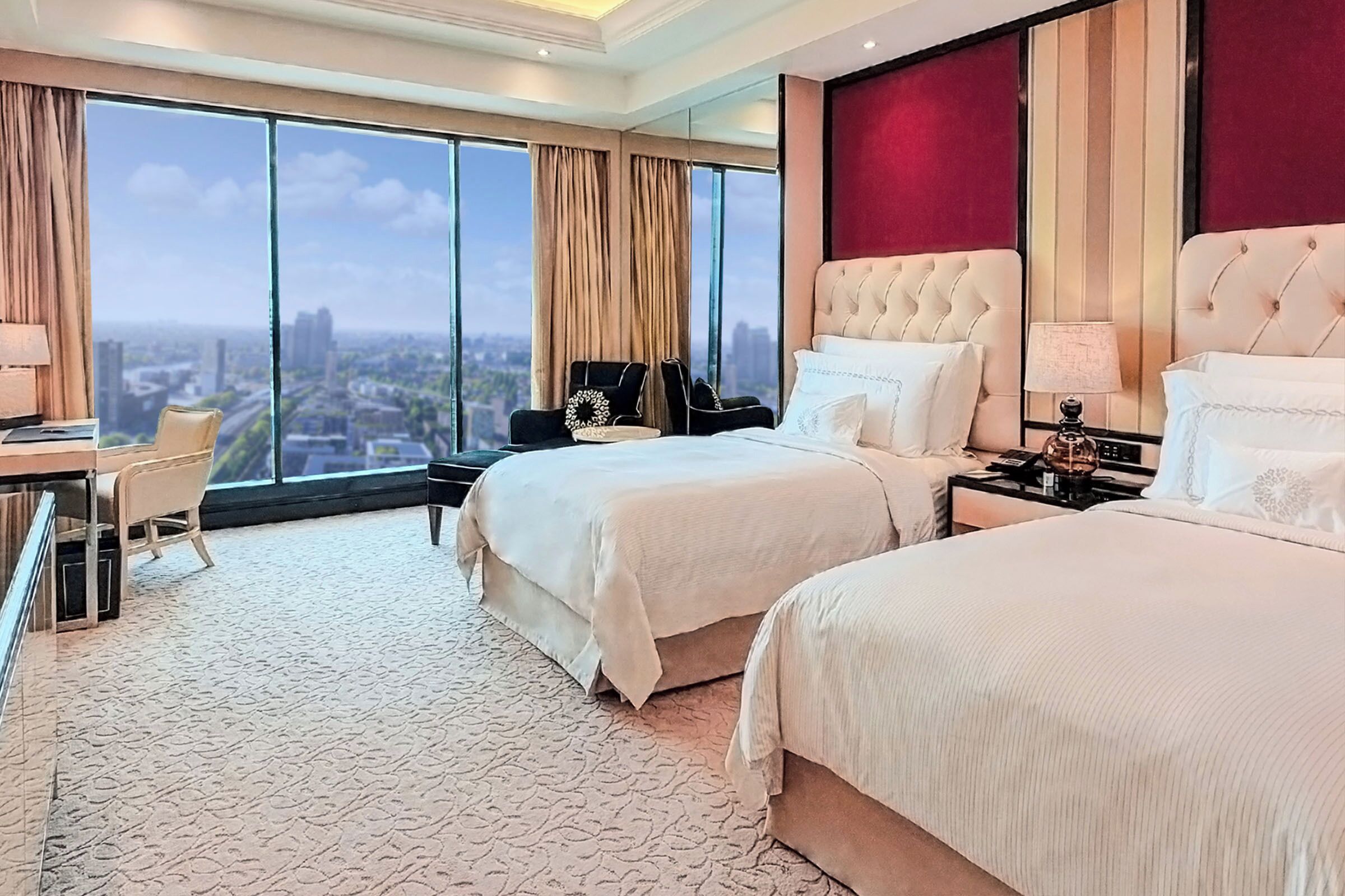 Ein Hotelzimmer mit zwei Betten, einem Schreibtisch, einem Sessel und einem großen Fenster mit Blick auf die Stadt.