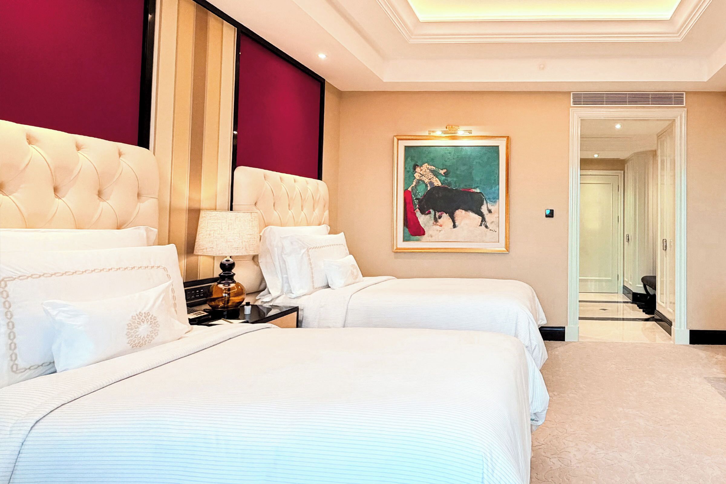 A hotel room with two beds, a nightstand, a lamp, and a painting on the wall.