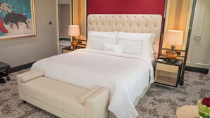 Una habitación de hotel con una cama grande, una mesita de noche con lámpara, un banco y un cuadro en la pared.