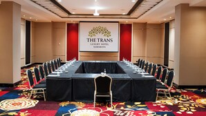 Un salón de conferencias en el Hotel Trans Luxury en Surabaya, con una larga mesa, sillas y una pantalla para proyector.