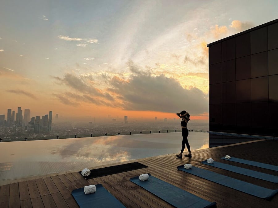 A rooftop with a city skyline view, yoga mats, and a person stretching.