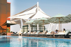 A poolside area with lounge chairs and umbrellas, a clear sky, and a modern building structure. - The Trans Luxury Hotel Surabaya (Surabaya)