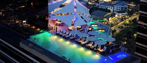 A rooftop pool area with lounge chairs and umbrellas, surrounded by buildings.