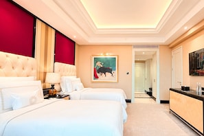 A hotel room with two beds, a desk, a lamp, a painting, and a door leading to another room. - The Trans Luxury Hotel Surabaya (Surabaya)