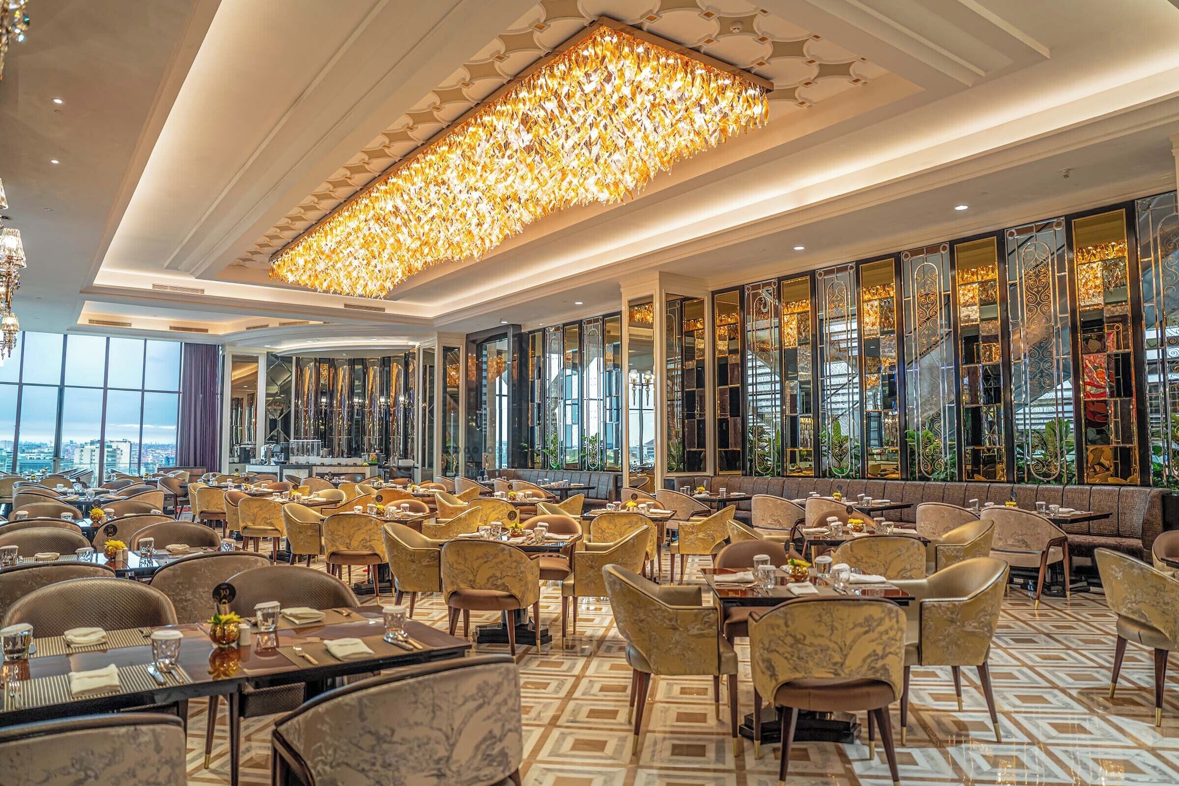 A spacious dining area with multiple tables and chairs, large windows, and a decorative ceiling light fixture.