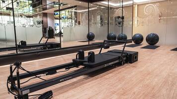 A Pilates reformer machine in a room with a wooden floor, large mirrors, and exercise balls.