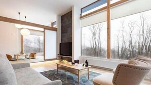 A modern living room with a large window, a fireplace, and a television. - Aoyama Lodge | 4BR Chalet in Kabayama | Stunning Mt. Yotei Views (Kutchan-cho)