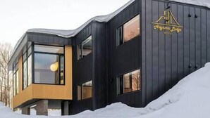 A modern hotel with a dark facade, large windows, and a logo on the side. - Aoyama Lodge | 4BR Chalet in Kabayama | Stunning Mt. Yotei Views (Kutchan-cho)