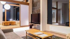 A modern living room with a wooden coffee table, a sofa, and a television mounted on the wall. - Aoyama Lodge | 4BR Chalet in Kabayama | Stunning Mt. Yotei Views (Kutchan-cho)