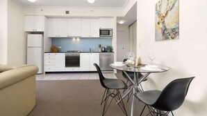 A compact kitchen with white cabinets, a microwave, and a dining area with a glass table and black chairs. - A Stylish Apt, City Views Next To Darling Harbour (Sydney)