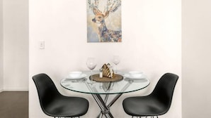 A dining area with a round glass table, two black chairs, and a painting of a deer on the wall. - A Stylish Apt, City Views Next To Darling Harbour (Sydney)