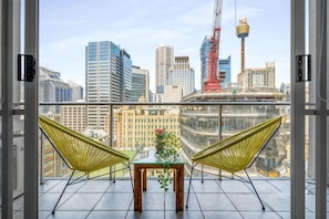 A balcony with two chairs, a table with a plant, and a cityscape view. - A Stylish Apt, City Views Next To Darling Harbour (Sydney)