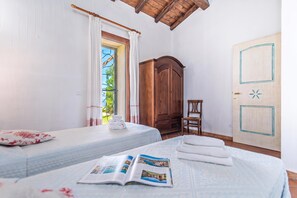 Ein Schlafzimmer mit einem Bett, einem Holzschrank, einem Fenster mit Vorhängen und einer Tür mit geometrischem Muster.