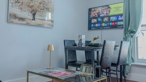 A modern dining area with a glass table, black chairs, a framed painting, and a TV displaying hotel amenities. - Rooftop/worktable/Netflix/Parking/Promo/longstay (London)