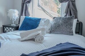Un lit bien fait, avec des serviettes pliées, des oreillers et un objet décoratif orné de plumes posé sur une table de chevet.