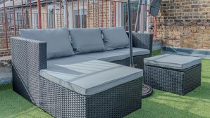 A wicker sofa with cushions and two ottomans in a garden setting. - Rooftop/worktable/Netflix/Parking/Promo/longstay (London)