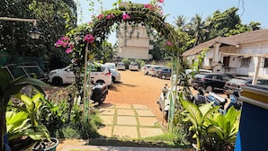 A courtyard with parked cars, a scooter, and a garden area with potted plants and a pergola with flowers. - Candolim Sands (Candolim)