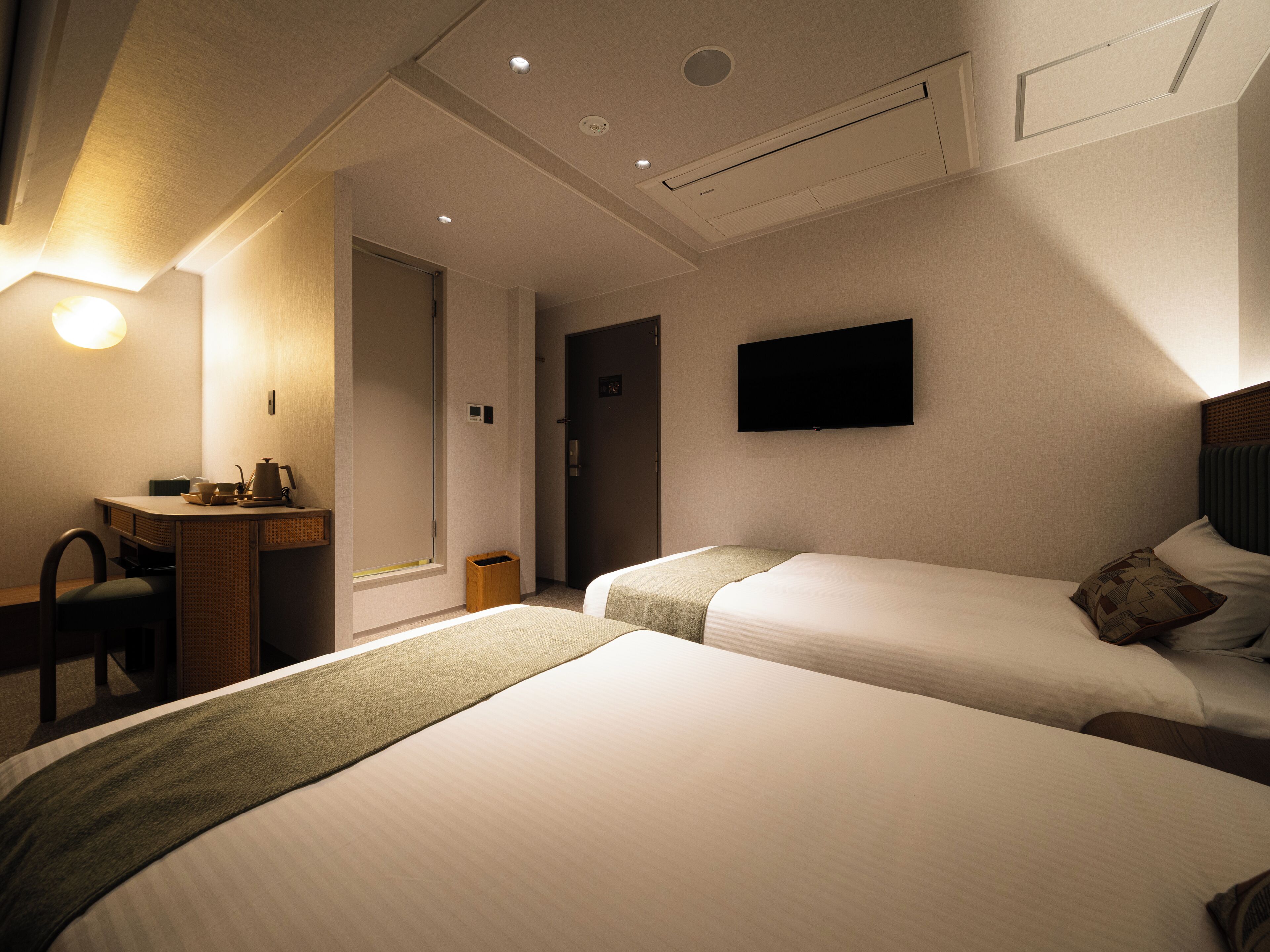 A hotel room with two beds, a desk, a chair, a television, and a window.