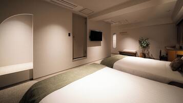Een hotelkamer met twee bedden, een flatscreen televisie, een klein tafeltje en een plant.