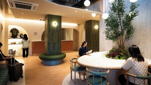 Um hall de hotel moderno com uma mesa de recepção, área de estar e uma grande planta.