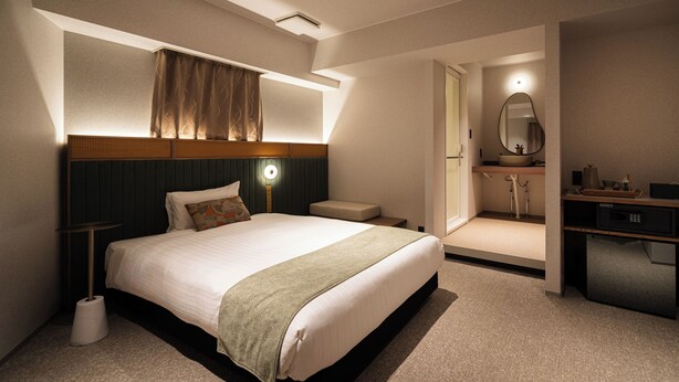 Quarto de hotel com uma cama grande, mesa de cabeceira e escrivaninha com um computador.