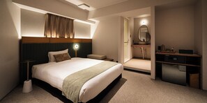Habitación de hotel con una cama grande, mesita de noche y un escritorio con computadora.