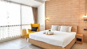 Una habitación de hotel moderna con cabecera de madera, una cama grande, un sillón amarillo y vistas a través de ventanales de gran altura.