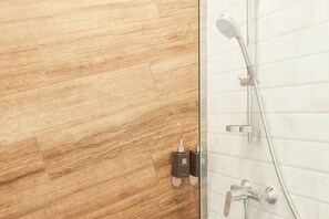 A bathroom with a wooden floor, a glass shower enclosure, and a white tiled wall. - Vann House Hua Hin (Hua Hin)