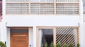 Un edificio de dos pisos con puerta de madera y ventanas con persianas horizontales.