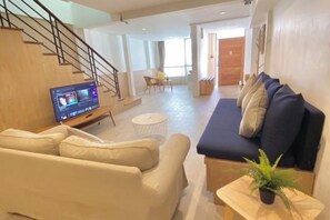 Una sala de estar moderna con sofá, mesa de centro y televisor. Se ve una escalera que sube a otro nivel.