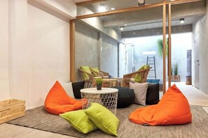 Un intérieur moderne avec un coin salon agrémenté de coussins orange et verts, une petite table ronde et un grand miroir qui reflète la pièce.