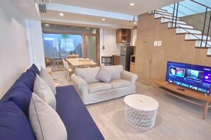 A modern living room with a sofa, a television, and a dining area in the background. - Vann House Hua Hin (Hua Hin)